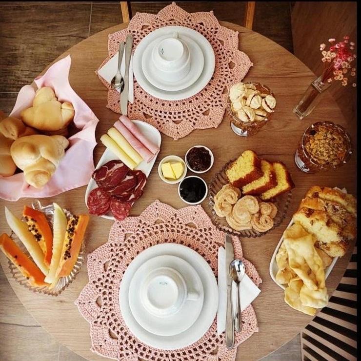 Café da manhã variado na CasAlta pousada, com pães, bolos, frutas, frios, bolachinhas, geleias, manteiga e xícaras e pratos postos