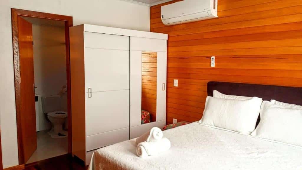 Quarto no Casas Ana. A cama é de casal e está à direita da foto. No seu lado esquerdo há um guarda-roupa. Há um ar-condicionado acima dele. A porta do banheiro está do lado esquerdo do guarda-roupa. Representa o post sobre airbnb em Canela.