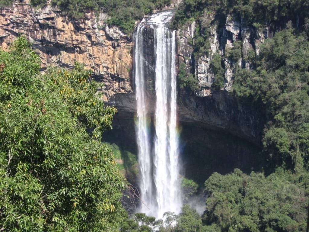 Cascata Caracol em Canela caindo sobre um penhasco cercado por uma floresta verdejante e formações rochosas.