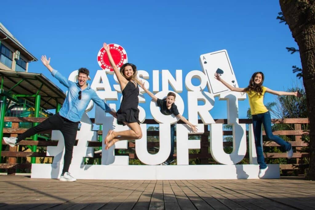 Quatro pessoas pulam de excitação em frente a uma grande placa com os dizeres "CASINO RESORT #EUFUI no no Cassino All Inclusive Resort Poços de Caldas.