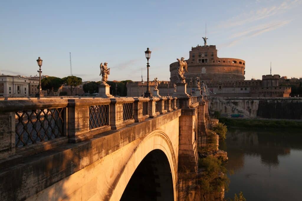 vista da ponte em pedra com diversas esculturas de anjos que leva até a fortaleza do Castelo de Santo Ângelo, com um grande anjo esculpido acima, em Roma