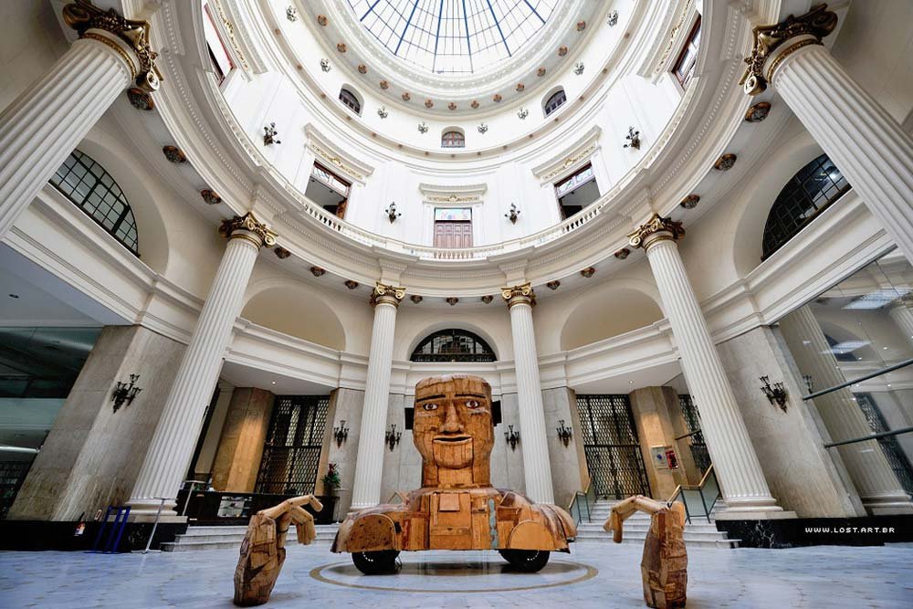 Centro Cultural Banco do Brasil com uma grande escultura de madeira de um robô com rosto e braços humanos, situada em um grande átrio com teto de vidro abobadado e colunas. Imagem para ilustrar o post sobre museus no Rio de Janeiro.