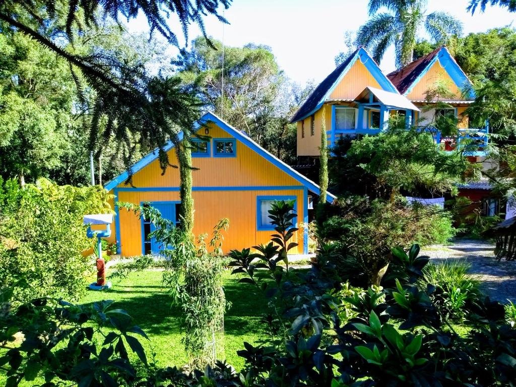 A imagem mostra uma cena tranquila ao ar livre com dois chalés do Residencial Saldanha cercados por vegetação exuberante