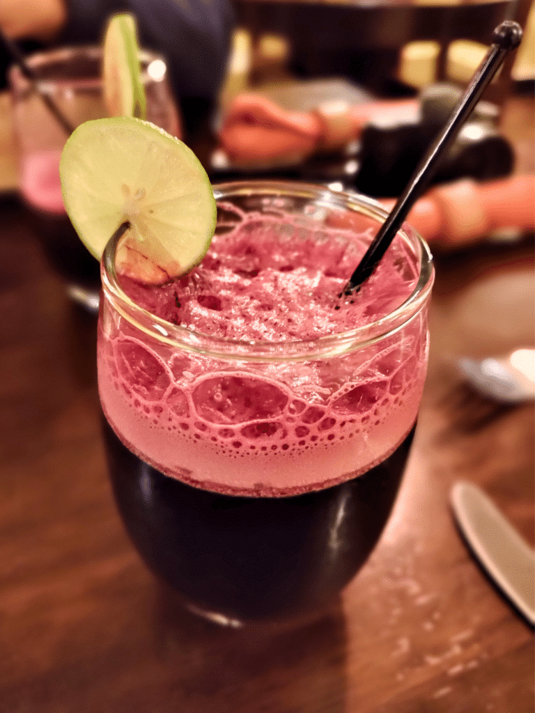 suco de chicha morada num copo de vidro contendo um líquido vinho, vermelho escuro, com uma fina rodela de limão cortada e presa na beirada do copo no restaurante el huacatay