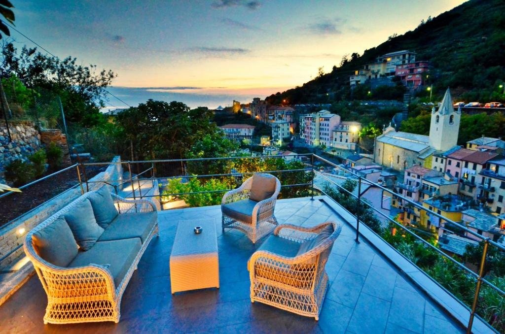 Parte do hotel com um sofá, duas poltronas e uma mesinha de centro ao ar livre com vista para as construções e montanhas da cidade, ilustrando post Hotéis em Cinque Terre. 