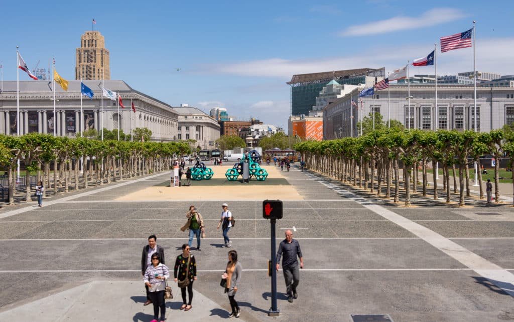 Civic Center durante o dia. Na foto está a parte da praça, com árvores em volta, as construções ao redor e algumas pessoas andando. 