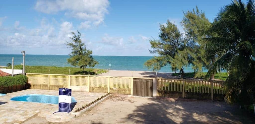 Área externa com piscina pequena e acesso a praia do Condomínio Village, Casa Cecília. Há um portãozinho baixo separando a propriedade de um gramado verde, com algumas árvores, e da areia fofa da praia