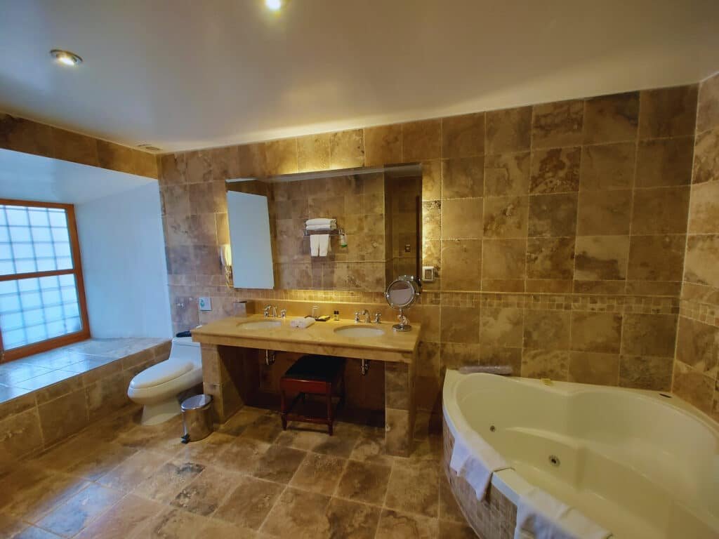 banheiro do costa del sol wyndham cusco com uma banheira de hidromassagem à direita, uma pia dupla ao centro da imagem e um vaso sanitário à esquerda, ao lado de uma janela