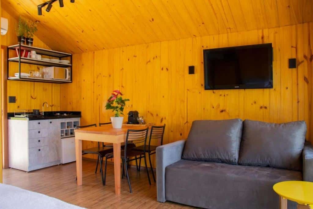 espaço da Cappio Pousada e Lazer com mini cozinha, equipada com frigobar, adega, pia, micro-ondas e mesa com cafeteira, além de sofá e TV ao lado
