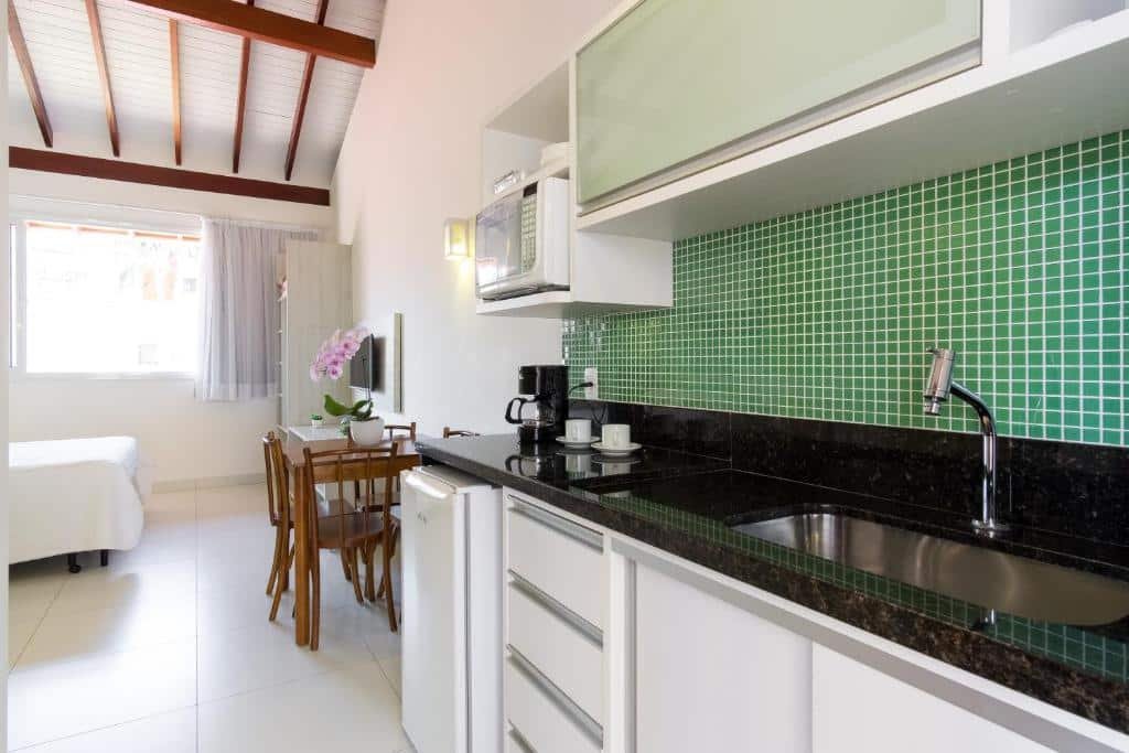 Mini-cozinha da Pousada Villa Peixes do Mar, uma pia em granito preto, uma torneira, uma cafeteira e xícaras, um móvel com gavetas, um micro-ondas, uma frigobar e uma pequena mesa com quatro cadeiras