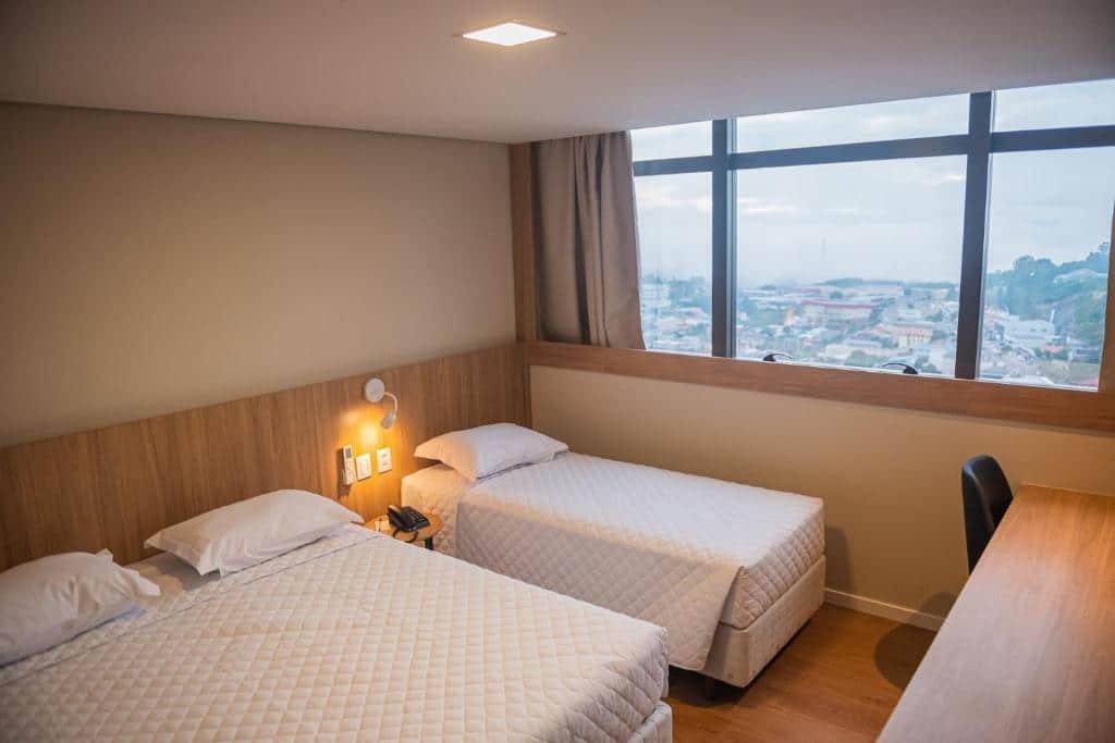 Quarto triplo, com cama de casal e uma cama de solteiro, além de mesa de trabalho com cadeira, janela de fora a fora na parede, e cortina blecaute, no Dall