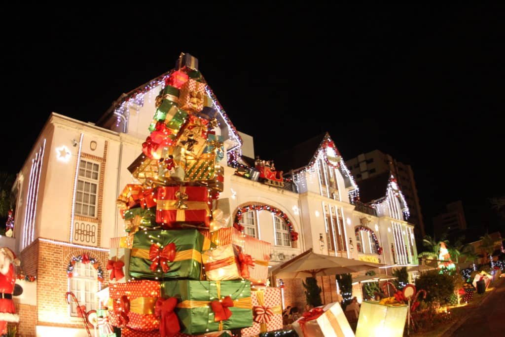 Na foto vemos a decoração de Natal da Vila Germânica Blumenau, com árvore montada de presentes e luzes típicas. Foto do site oficial Parque Vila Germânica.