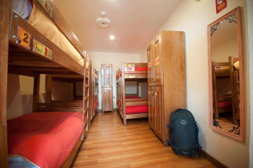 dormitorio do Pariwana Hostel Cuscocom três beliches no lado esquerdo da imagem. No lado direito há um espelho vertical e um armário