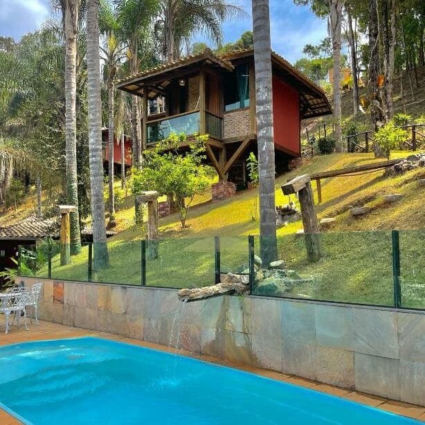 Piscina da Eco Pousada VerDivino, com bastante natureza em volta e um chalé com varanda ao fundo