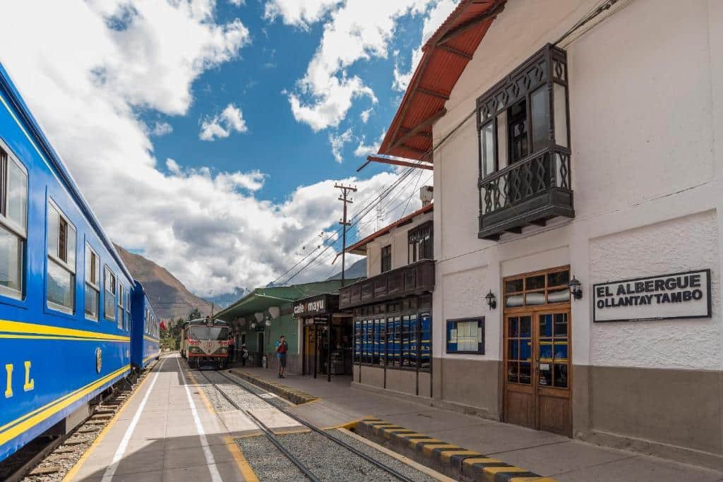 área da ferrovia em Ollantaytambo, com uma parte do trem da PeruRail aparecendo no canto esquerdo da imagem. Do outro lado dos trilhos é possível ver a construção do El Albergue Ollantaytambo.