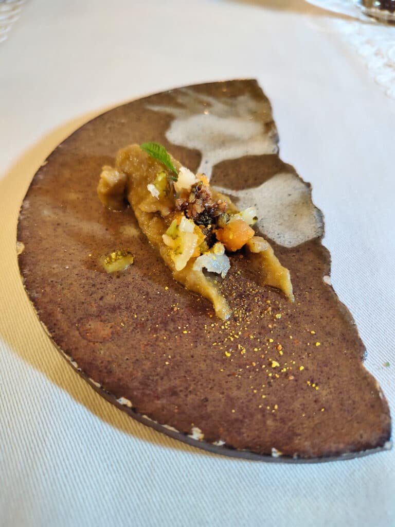 prato de pedra em formato meia lua com um pequeno aperitivo de batatas em cima