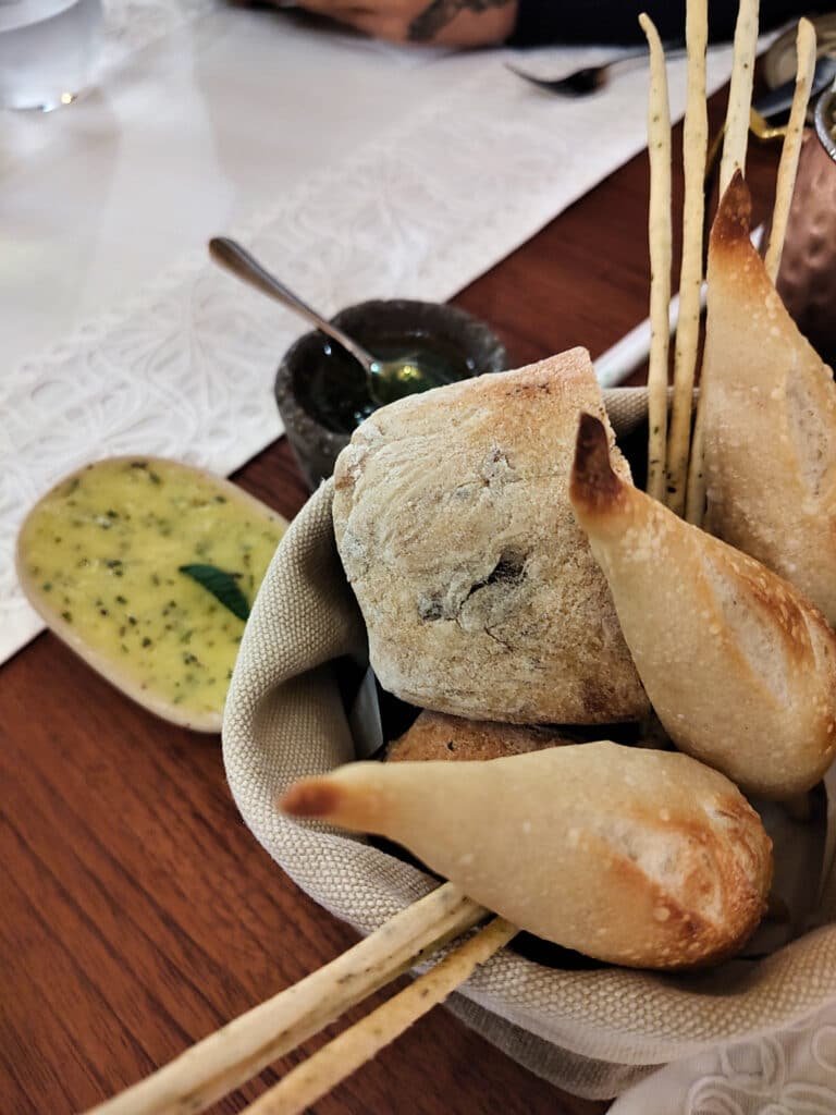 cesta de pães típicos peruanos em diferentes formatos, acompanhados de um pequeno potinho de manteiga temperada ao lado