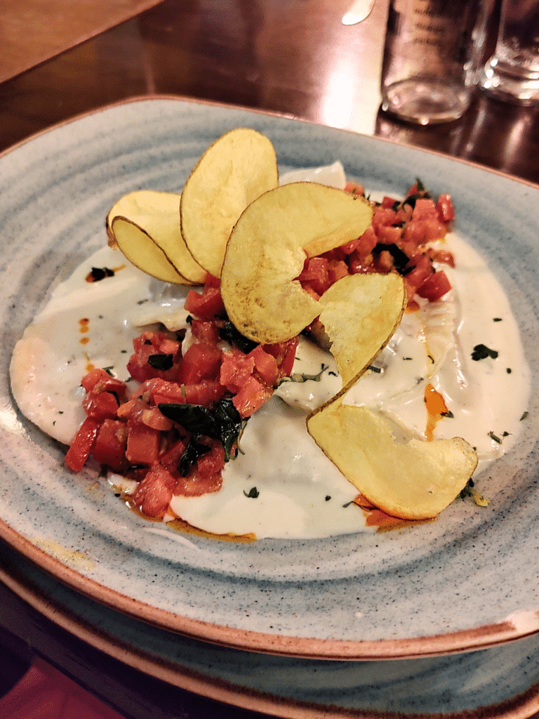 prato quadrangular azul com massa ao molho branco, tomates picados formando um caminho no meio do prato e uma batata cortada e assada em espiral bem cima do molho no restaurante el huacatay