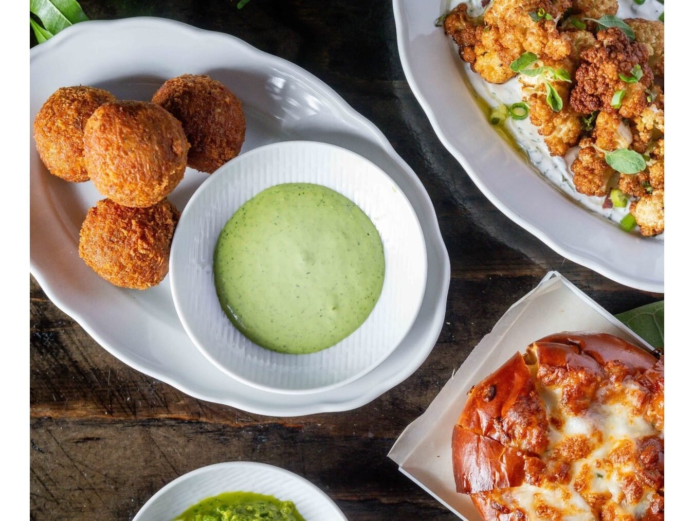 Pratos de couve-flor frita, arancini com molho verde, pão sírio com queijo e um pequeno prato de chutney em uma mesa de madeira no Restaurante Emesh em Tel Aviv.