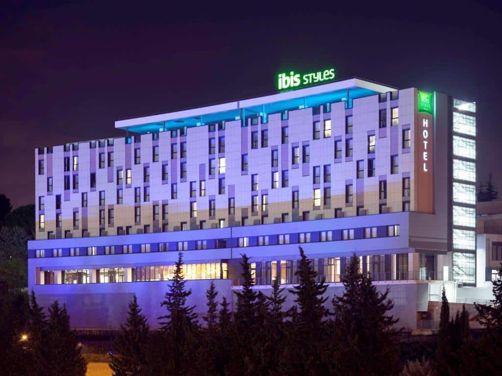 fachada do Ibis Styles Roma Eur à noite, com várias janelinhas na parede branca e com detalhes em azul e bem iluminado, sendo um dos hotéis Ibis em Roma