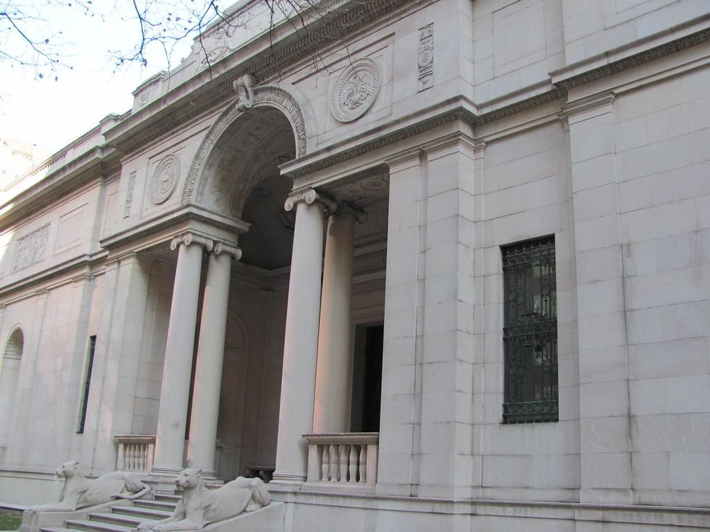Exterior do Morgan Library & Museum com colunas, um arco central e duas estátuas de leões ladeando os degraus de entrada.