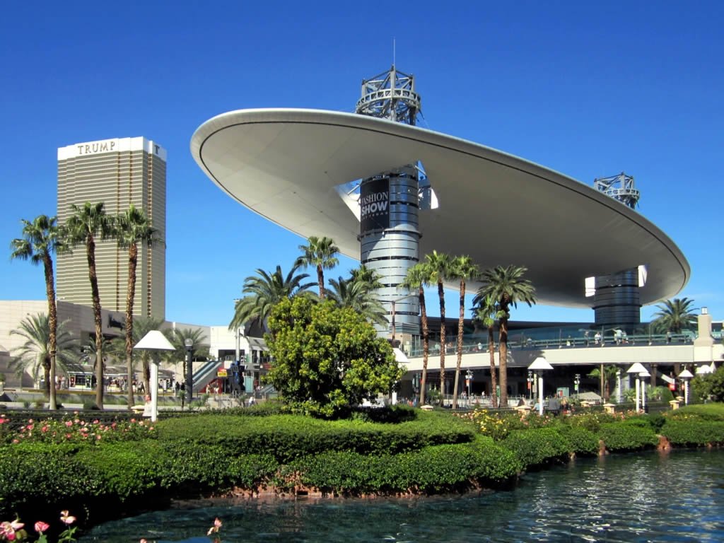 Vista externa do Fashion Show Mall. Uma grande estrutra que se parece com uma nave espacial é apoiada pela estrutura do shopping. Ao redor estão outros edifícios e um lago.