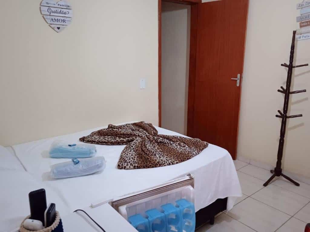 Quarto da Fazenda Lagoa Azul com uma cama com um cobertor de estampa de leopardo e dois travesseiros. Um cabideiro de madeira fica ao lado de uma porta aberta.