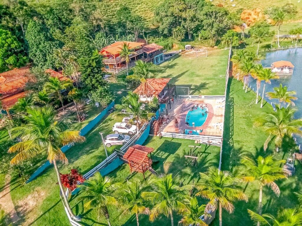 Vista aérea da Fazenda Lagoa Azul, um dos hotéis fazenda no Rio de Janeiro, com piscina, cercada por árvores e grama. Há um lago e vários prédios com telhados vermelhos.