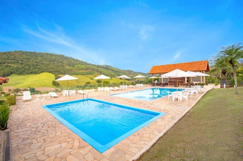 Duas piscinas ao ar livre do Filimahalo Hotel, ao redor cadeiras e guarda-sóis, no fundo as montanhas.