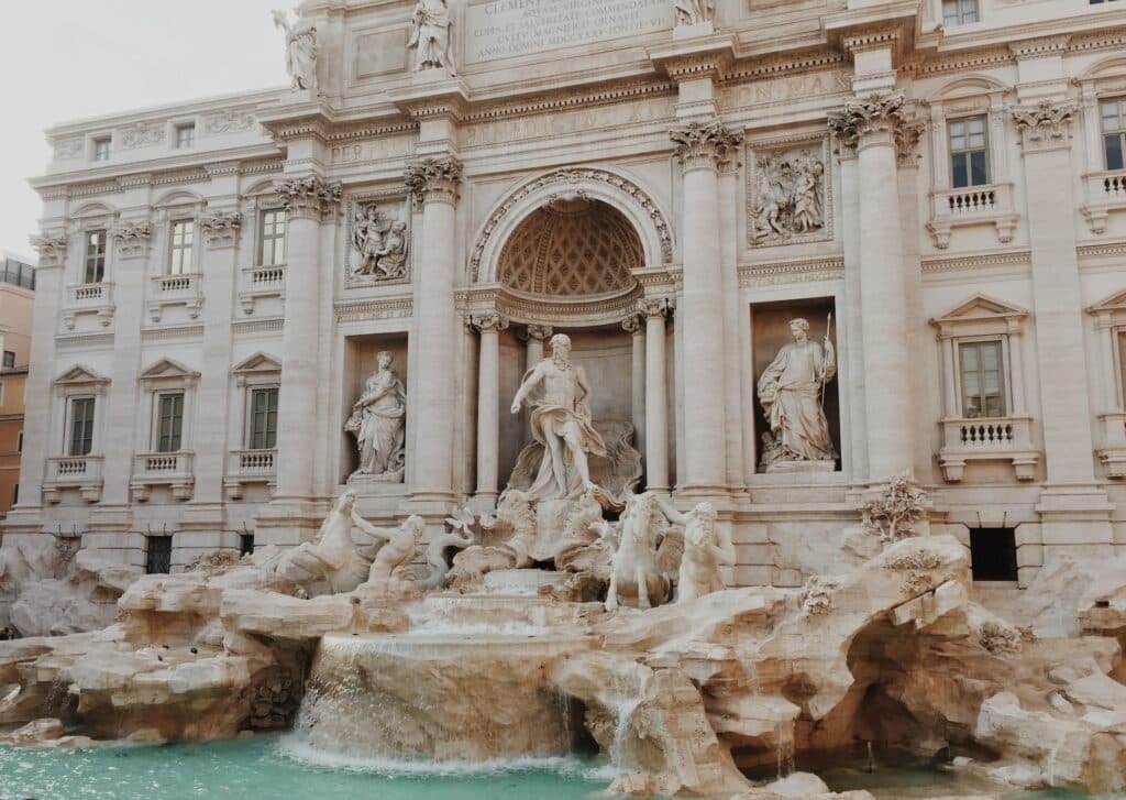 vista da fachada com colunas gregas da Fontana Di Trevi, em Roma, com águas claras e esculturas de Netuno ricamente trabalhadas em estilo clássico em branco