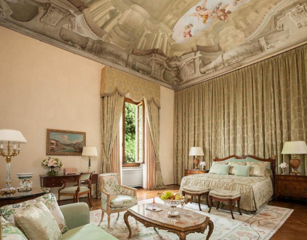Quarto do Four Seasons Hotel Firenze, de 76 m², parecendo uma acomodação real, com decoração clássica e super elegante, contando com móveis de época, cortinas altas e pinturas no teto