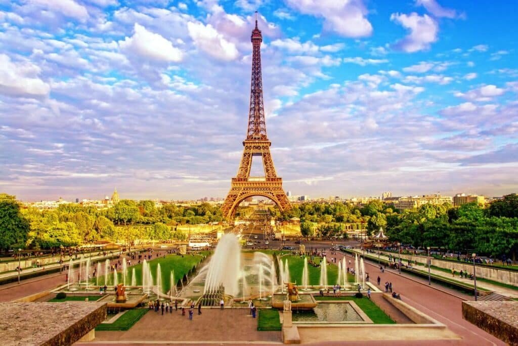 A Torre Eiffel se destaca nos passeios em Paris, com fontes e pessoas em primeiro plano, sob um céu parcialmente nublado. Esse é um dos pontos turísticos de Paris.