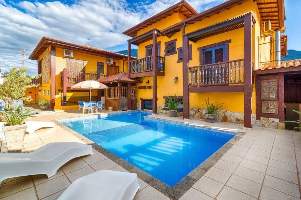 Imagem da área de lazer da Aldeia Da Lagoinha durante o dia com duas cadeiras do lado esquerdo da imagem a frente no meio a piscina e ao fundo do lado direito a estadia.