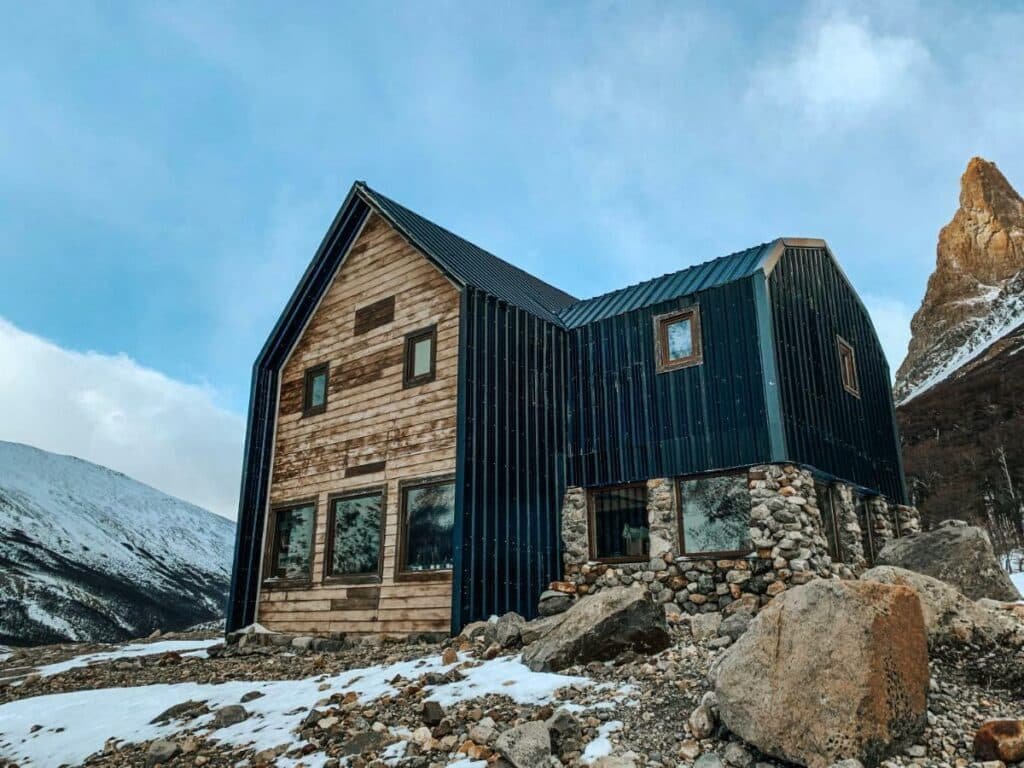 Frente do Puesto Cagliero - Refugio de montaña durante o dia com a propriedade no meio em volta de pedras e neve.