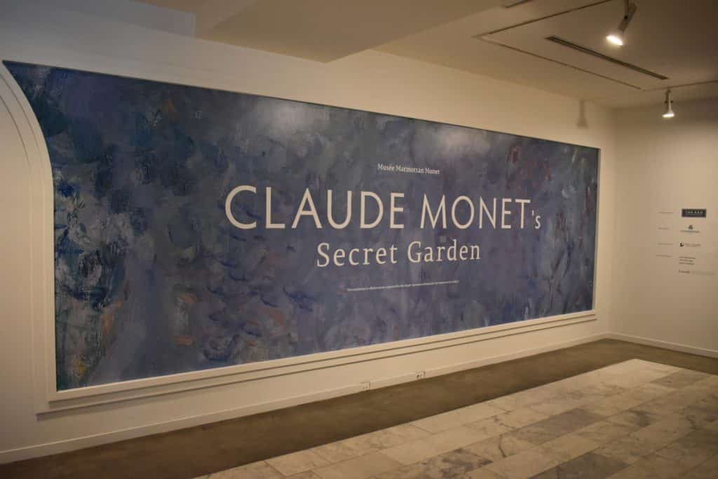 Entrada dao Vancouver Art Gallery com uma grande placa que diz "Jardim Secreto de Claude Monet" em um fundo azul texturizado.
