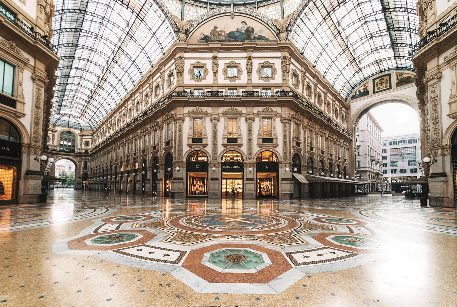 Interior da Galleria Vittorio Emanuele II com teto de vidro ornamentado, piso de mosaico decorativo e arquitetura clássica. É uma ótima opção de o que fazer em Milão.