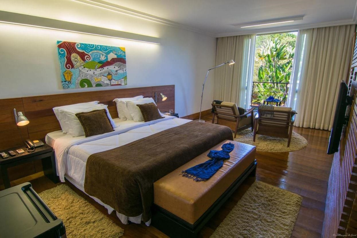 Um quarto do Garden Hill Hotel e Golfe com uma cama grande, um banco acolchoado, uma área de leitura com cadeiras perto da janela e obras de arte modernas na parede.