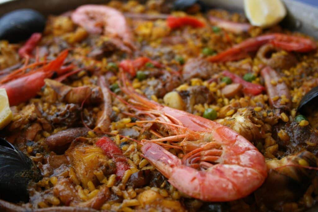 Close de um prato de paella com camarão, mexilhões, arroz e fatias de limão.