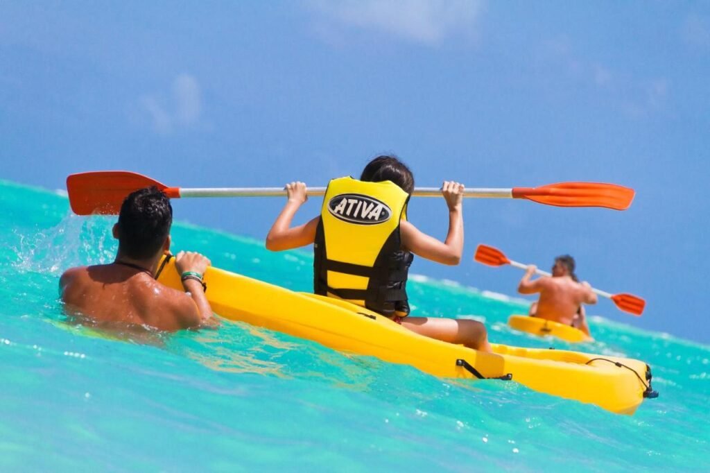 Três pessoas andando de caiaque em caiaques amarelos brilhantes em águas azul-turquesa sob um céu azul claro no Grand Oca Maragogi All Inclusive Resort.