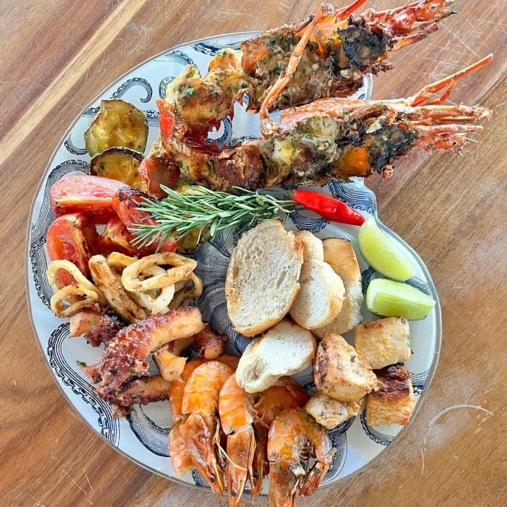 Foto de um prato chamado grelhada mista al’mare, do restaurante Manito Praia em Porto Seguro, O que vemos no prato é uma grelhada com alimentos mistos como pães, camarões, legumes, ervas, etc.