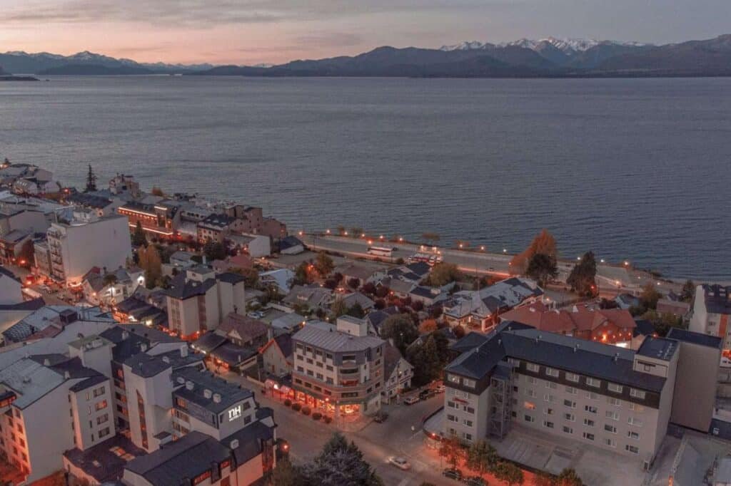 Vista aérea do Hampton By Hilton Bariloche, com diversos prédios ao redor e no fundo o lago.