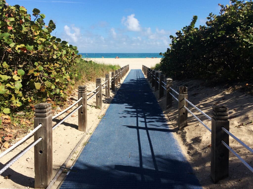 Caminho para acessar a praia Haulover Beach. Depois dele está a faixa de areia com poucas pessoas e o mar bem azul. Essa é uma opçõa não tão conhecida de o que fazer em Miami.