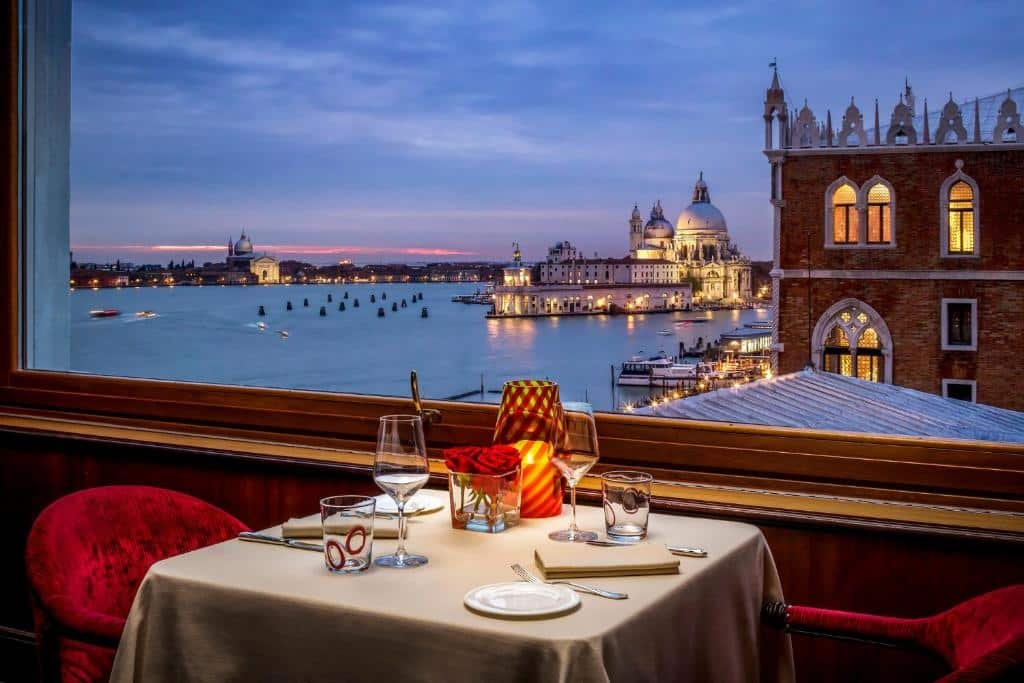 Uma mesa de jantar à luz de velas para dois com vista para um canal veneziano e edifícios históricos ao pôr do sol para representar um dos melhores lugares para lua de mel