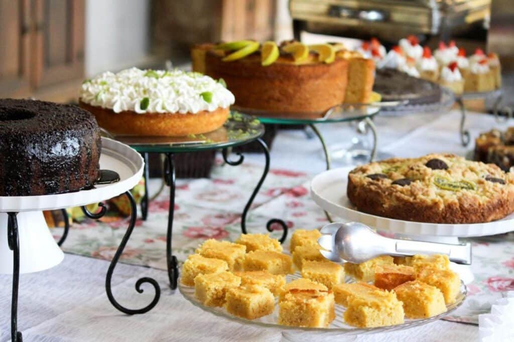 Uma mesa com vários bolos e sobremesas, incluindo bolos de chocolate e cobertos com frutas, expostos em suportes e pratos no Hotel Fazenda Casarão do Vale.