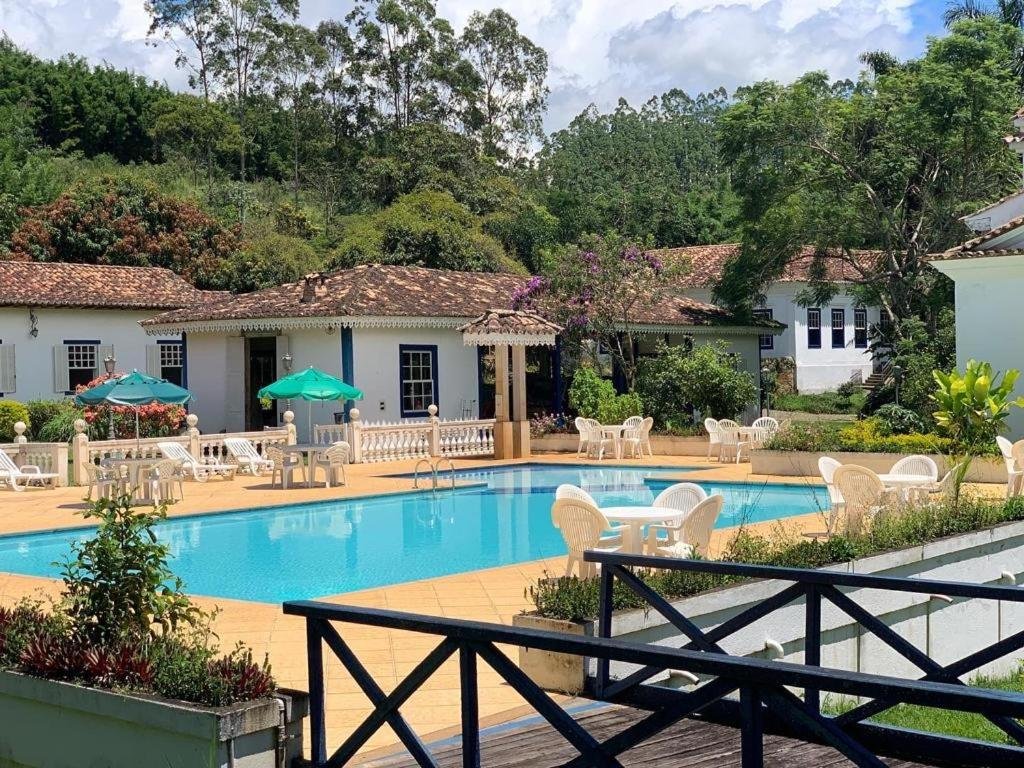 Área de piscina ao ar livre do Hotel Fazenda Florença, um dos hotéis fazenda no Rio de Janeiro, com móveis de jardim, cercada por vegetação e edifícios em estilo colonial sob um céu parcialmente nublado.