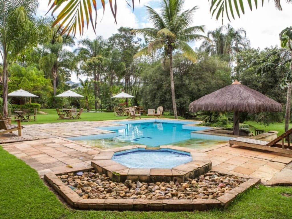 Um quintal com piscina e uma pequena jacuzzi redonda, cercada por lajes de pedra, grama, espreguiçadeiras e palmeiras no Hotel Fazenda Igarapés.