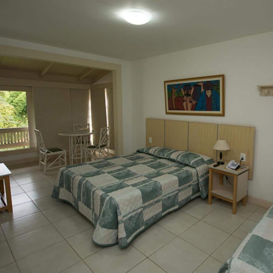 Um quarto do Hotel Fazenda Rochedo com uma cama de casal, uma pequena mesa de jantar com cadeiras, um criado-mudo e uma pintura emoldurada na parede.