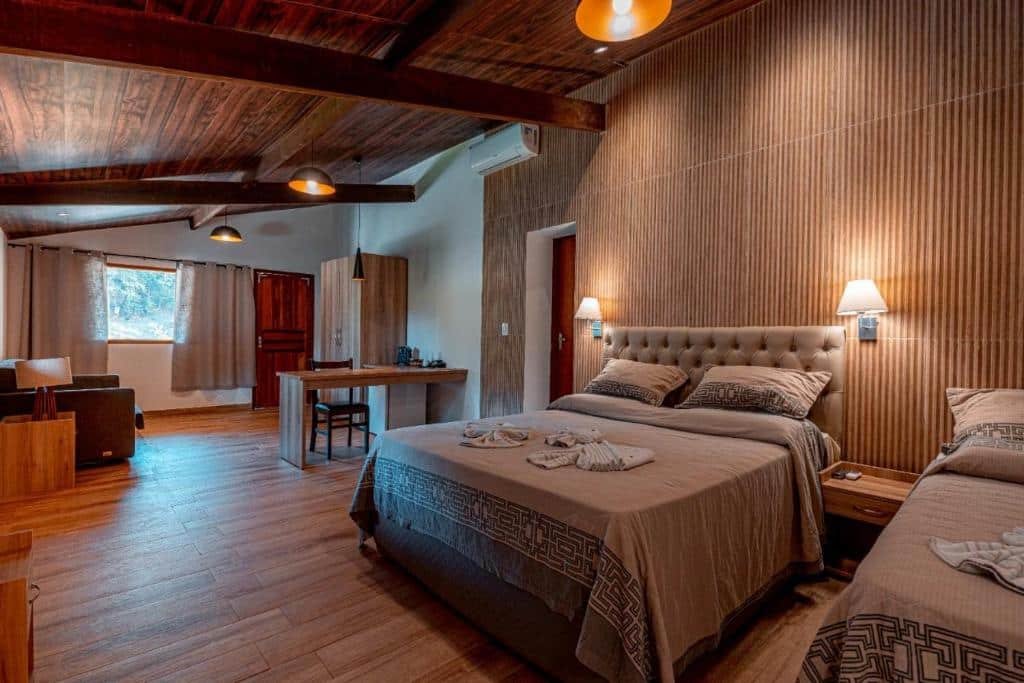 Um quarto do Hotel Fazenda Santa Barbara, um dos hotéis fazenda no Rio de Janeiro, com duas camas de casal, teto de madeira, uma escrivaninha e uma área de estar. A luz natural entra por uma janela.