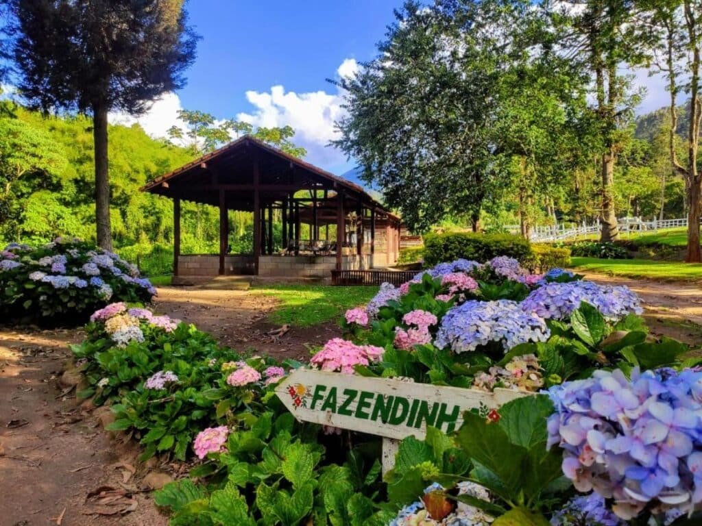Um mirante cercado por hortênsias floridas em um jardim exuberante, com uma placa dizendo "Fazendinha" em primeiro plano no Hotel Fazenda São Moritz, um dos hotéis fazenda no Rio de Janeiro.