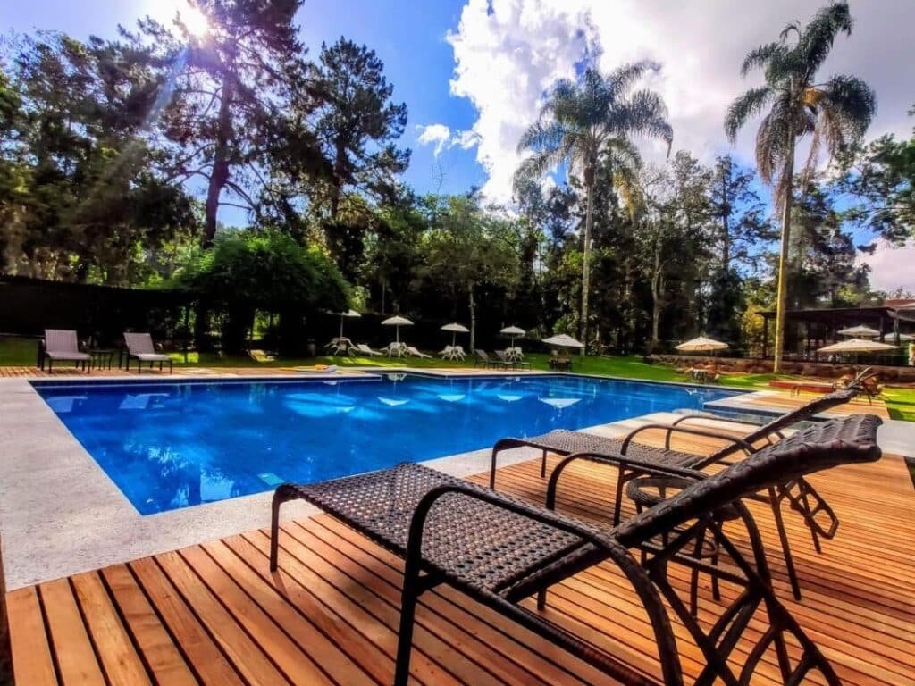 Piscina ao ar livre no Hotel Fazenda São Moritz com espreguiçadeiras em um deck de madeira, cercada por árvores e palmeiras sob um céu azul com nuvens.